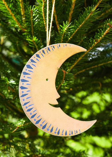 Decorative gold moon-shaped ornament with blue patterns hanging on a Christmas tree.