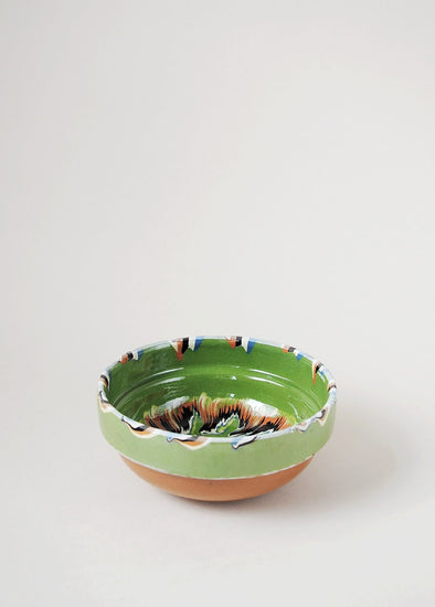 Ceramic bowl decorated in traditional Romanian pattern. Green base with patterned glaze in orange, blue, yellow, cream and black.
