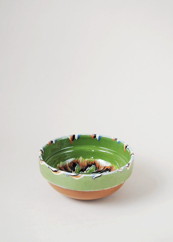 Ceramic bowl decorated in traditional Romanian pattern. Green base with patterned glaze in orange, blue, yellow, cream and black.