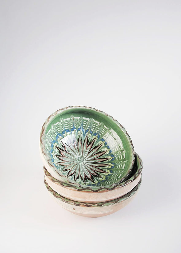 Three ceramic bowls in a stack. They are decorated in traditional Romanian pattern. Green base with swirls of black, blue, white, red and yellow.
