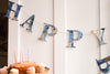 A garland of paper letters strung across a white door. The letters spell out Happy Birthday and are made from blue patterned papers.