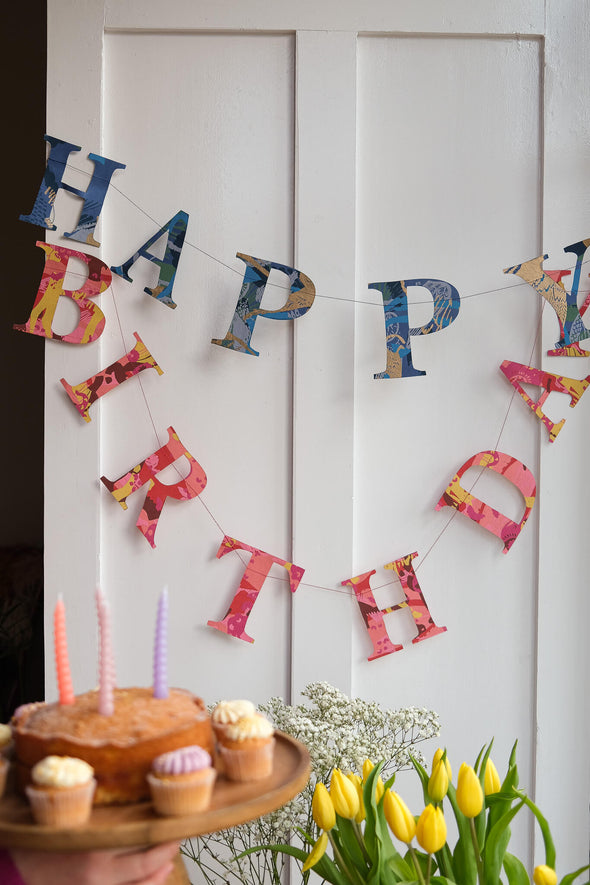 A garland of paper letters strung across a white door. The letters spell out Happy Birthday and are a mix of blue and red patterned papers.