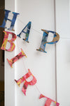 A garland of paper letters strung across a white door. The letters spell out Happy Birthday and are a mix of blue and red patterned papers.