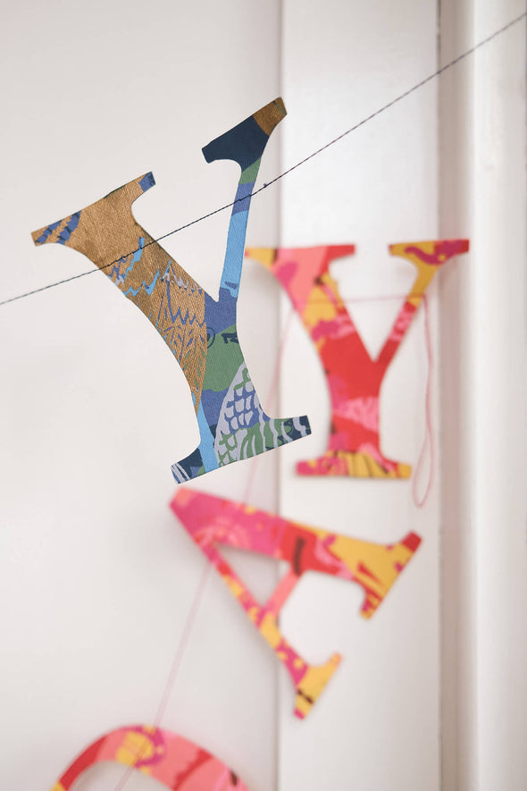 Close up of a garland of paper letters strung across a white door. The letters spell out Happy Birthday and are a mix of blue and red patterned papers.