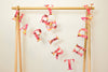 A garland of paper letters strung across a wooden frame. The letters spell out Happy Birthday and are a mix of pink, yellow and red patterned papers.