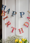 A garland of paper letters strung across a white door. The letters spell out Happy Birthday and are a mix of blue and red patterned papers.