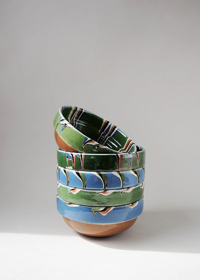 Stack of green and blue ceramic bowls decorated in traditional Romanian pattern. 