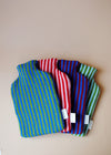 Four knitted hot water bottle covers spread out in a fan. Each has a striped design in different colours.