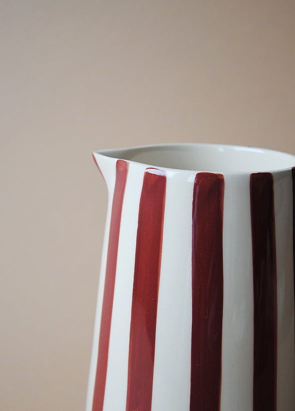 Close up of a burgundy and white striped ceramic jug.