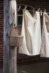 A tea towel hanging from a washing line in the sun. The towel is cream with a brown interwoven stripe pattern.