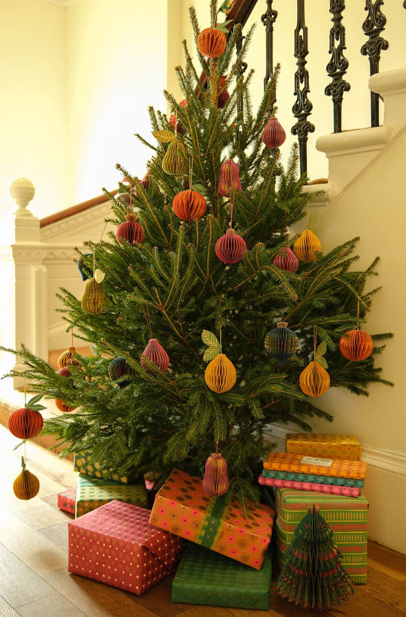 A Christmas tree covered in hanging paper fruit decorations. Colourfully wrapped presents lie under the tree.