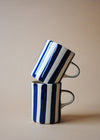 Two ceramic mugs in a stack with painted deep blue stripes.