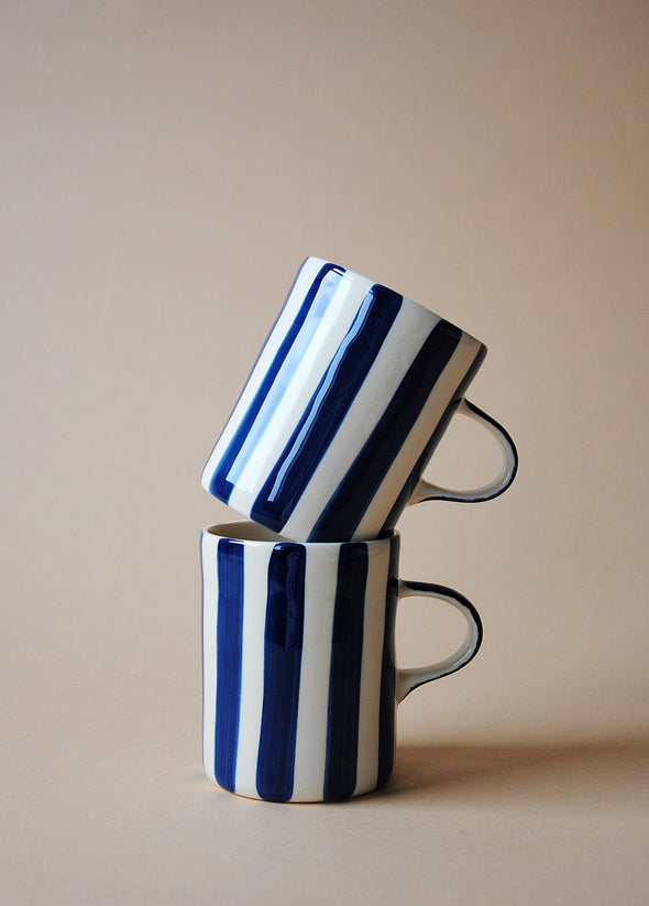 Two ceramic mugs in a stack with painted deep blue stripes.