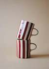 Two ceramic mugs in a stack with painted burgundy stripes.