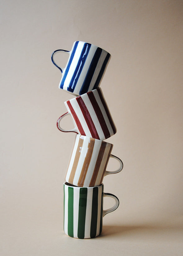 Four mugs stacked on top of each other. Each has a different colour painted stripe design in green, light brown, burgundy and blue.