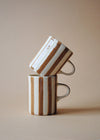 Two ceramic mugs in a stack with painted light brown stripes.