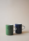 One blue and white striped ceramic mug and one green and white striped ceramic mug sitting next to each other.