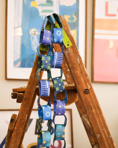 Blue and yellow patterned paper chain hanging from the top of a wooden step ladder.