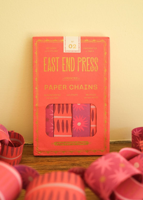 Red packet of East End Press paper chains on a wooden surface with pink paper chains around.