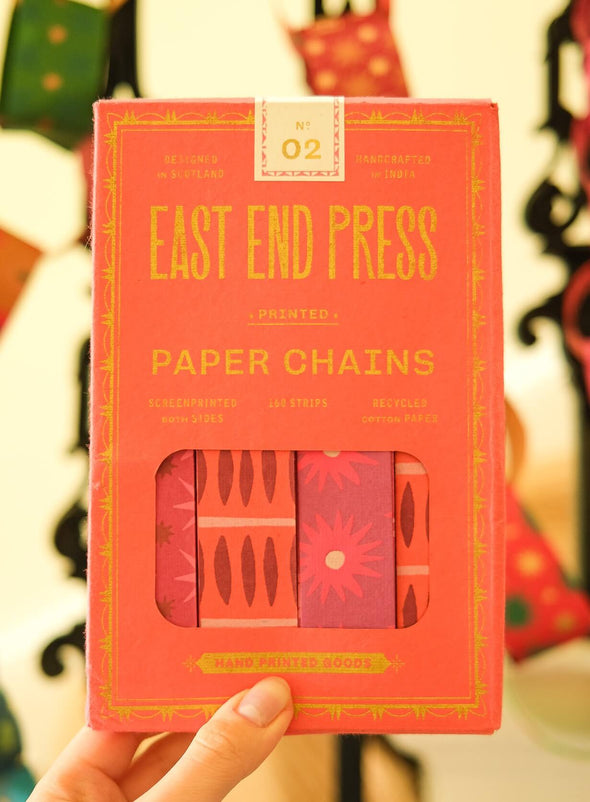 Red packet of East End Press paper chains held by a hand with a blurred background