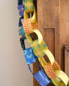 Two paper chains hanging down the corner of a wooden mantelpiece. One is yellow and green and the other is shades of blue.