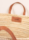 Close up of a basket bag with short tan leather handles.