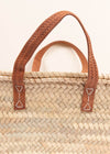 Close up of a basket bag with short tan leather handles.