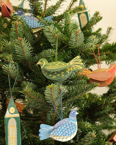 Green partridge decoration hanging from a Christmas tree surrounded by other decorations including a robin, blue doves and a green steeple.