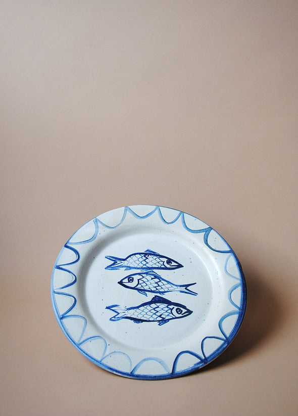Ceramic plate with a white glaze and cobalt blue painted illustration of three sardines.