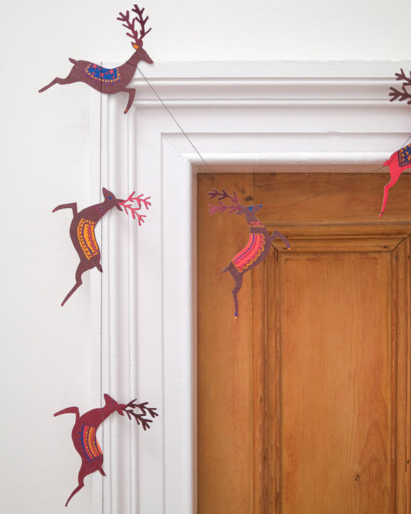 A paper garland featuring brown reindeer sewn on cotton string. The garland is strung over the corner of a door.