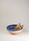 Pair of wooden salad hands resting in a ceramic bowl with blue glaze.