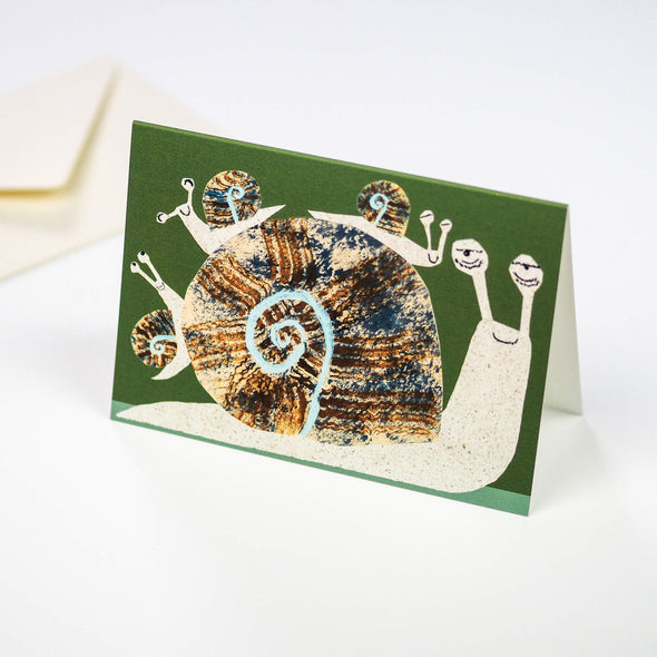 A greetings card depicting a large snail with three smaller snails climbing on its shell. The background is a deep green.