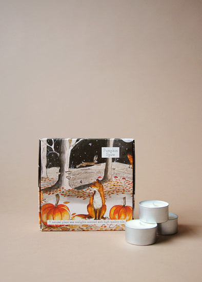 Square box illustrated with a sitting fox and a pumpkin either side. Trees and a leaping hare are in the background. Next to the box sits three tea lights. 