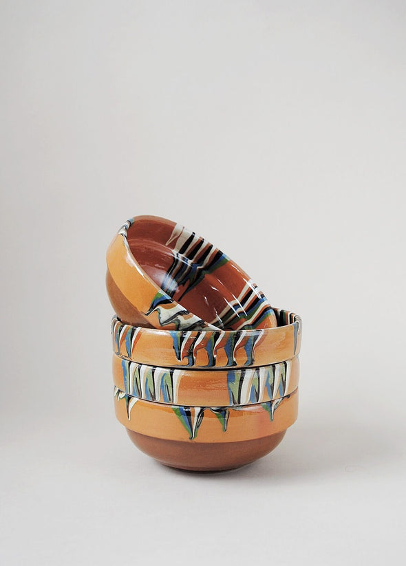 Stack of ceramic bowls decorated in traditional Romanian pattern. Terracotta base with a striped design in cream, green and blue.