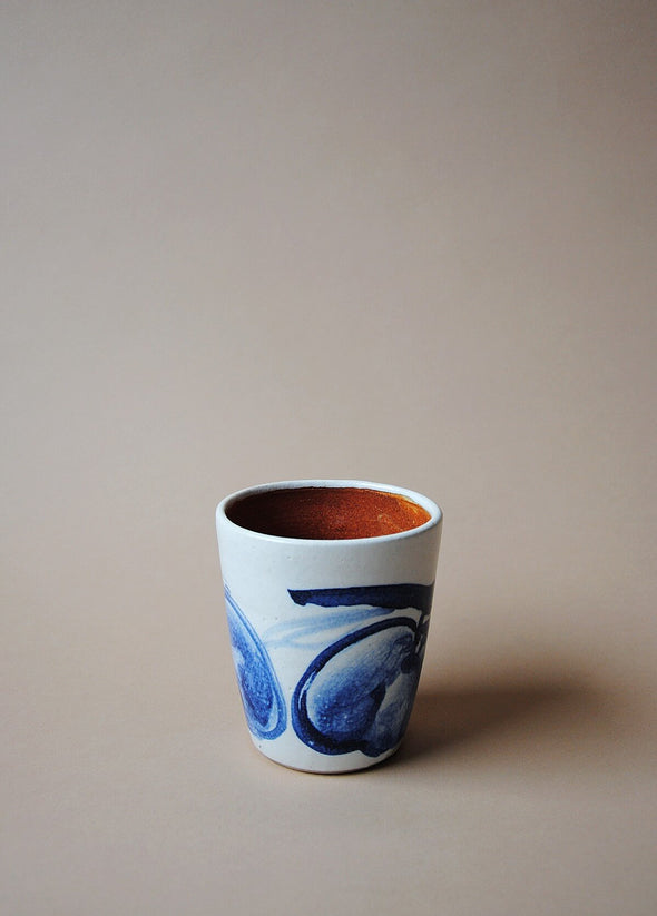 Ceramic tumbler in a white glaze with a blue hand painted design of apples.