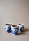 Three ceramic tumblers in a white glaze with a blue hand painted design of apples.