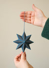 Hand holding a blue star-shaped ornament against a neutral background