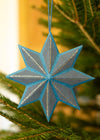 Blue star-shaped ornament hanging on a Christmas tree branch.