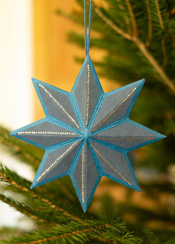 Blue star-shaped ornament hanging on a Christmas tree branch.