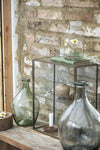 A glass tabletop cabinet containing knick knacks. Either side of the cabinet sits a teardrop shaped glass vase, one in a green coloured glass and the other grey.