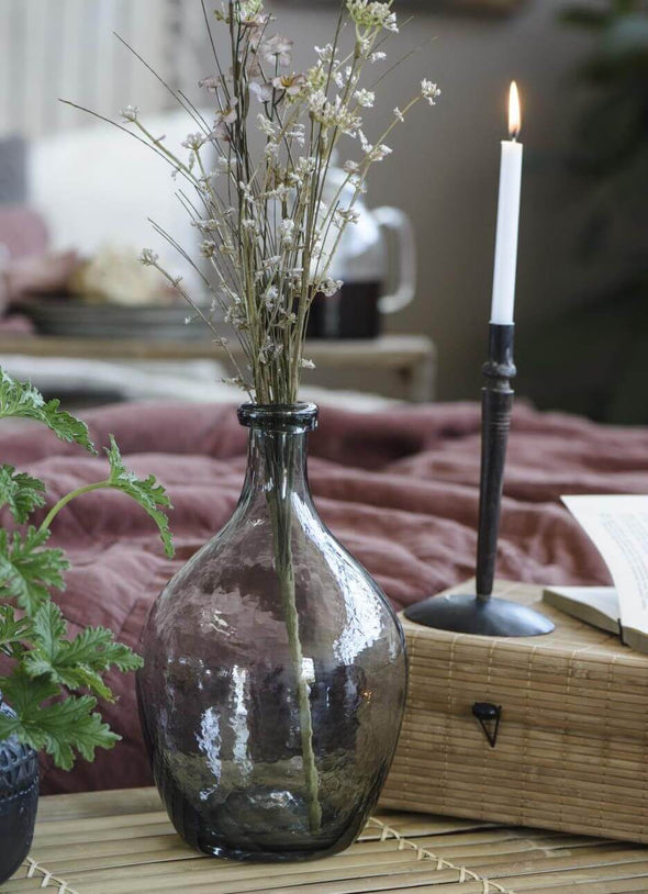 Grey glass teardrop shaped vase containing a few dried stems. 