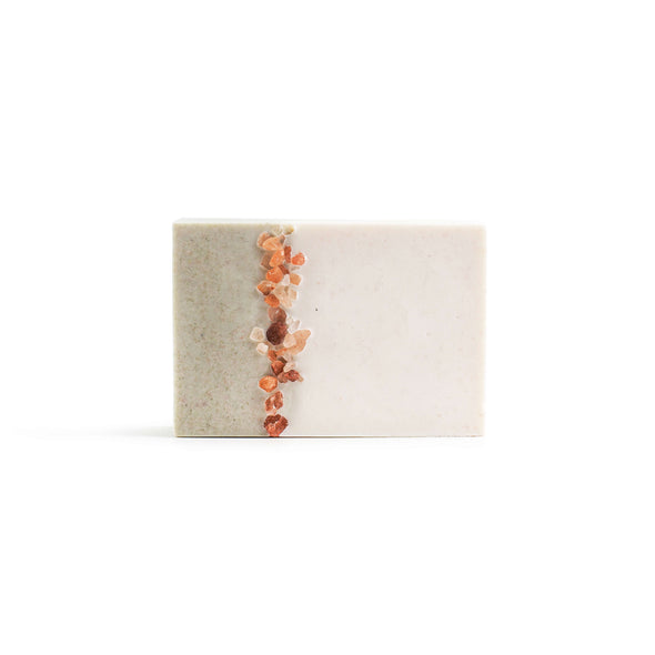 A rectangular soap which is two thirds white and one third pale green. Pink himalayan salt grains lie along the join between the two colours.