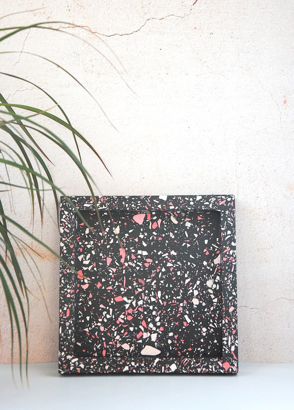 Terrazzo square tray handmade by Katie Gillies using jesmonite. It has a black base and red, pink and white chips. It is twenty centimetres by twenty centimetres and is two centimetres thick.