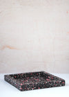 Terrazzo square tray handmade by Katie Gillies using jesmonite. It has a black base and red, pink and white chips. It is twenty centimetres by twenty centimetres and is two centimetres thick.