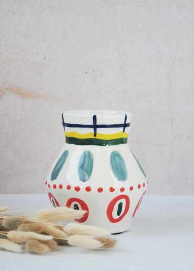 Ceramic vase with a white base and hand painted pattern of bold brush strokes in the colours green, red, blue and yellow. Height fifteen centimetres, width twelve centimetres.