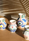 Group of four ceramic vases. All have a white base and are hand painted with bold brushstrokes using the colours blue, green, yellow, red and orange. Three of the vases have a height of fifteen centimetres and a width of twelve centimetres. One is larger at a height of nineteen point five centimetres and width of sixteen centimetres.