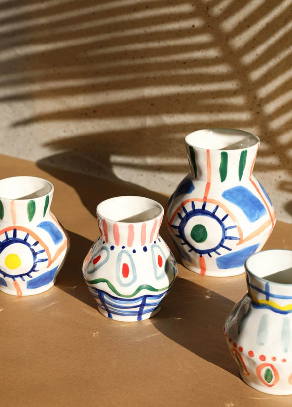 Group of four ceramic vases. All have a white base and are hand painted with bold brushstrokes using the colours blue, green, yellow, red and orange. Three of the vases have a height of fifteen centimetres and a width of twelve centimetres. One is larger at a height of nineteen point five centimetres and width of sixteen centimetres.