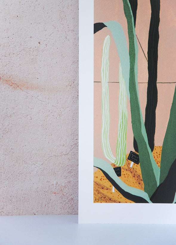Close up of a corner of an art print by Rachel Victoria Hillis. Depicting various green cacti on a pale pink background and sandy floor.