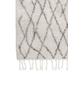 Close up corner of a black and white bathmat featuring an interlocking diamond design and tassels either end.