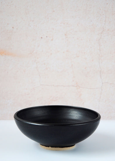 Footed bowl in a soft matte black glaze, handmade by Dor and Tan using local Cornish clay. The bowl is five centimetres high and sixteen centimetres wide.